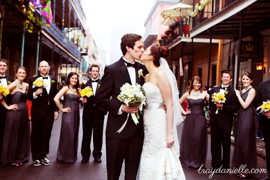 wedding party with bride and groom kissing in front