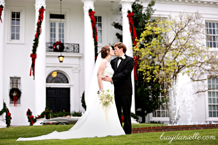 bride and groom kissing in front of mansion