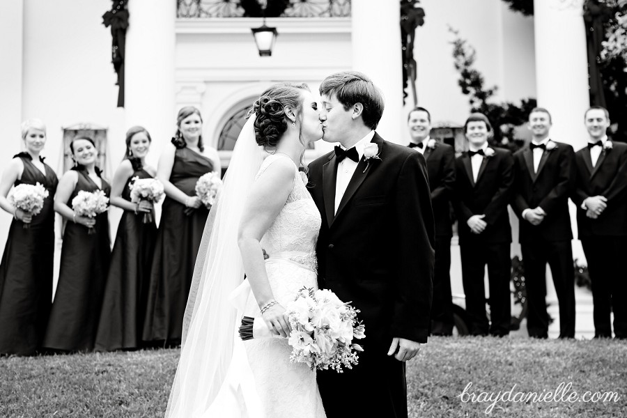 bride and groom kissing with wedding party in background